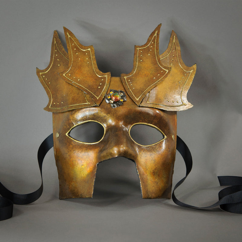 The Copper Warrior Bauta Masquerade mask is Inspired by medieval armor of the Renaissance. With it's masculine lines, this mask is particularly popular for men and is a lightweight and comfortable mask that is perfect for Halloween and Masquerade events. Mask is treated in shades of gold and copper with Dragon Wing panel armor, metal findings and assorted polished gems.  Handmade in the USA using traditional Venetian paper-mache techniques. Lined with hypoallergenic stretch velvet for comfort. Detail view.