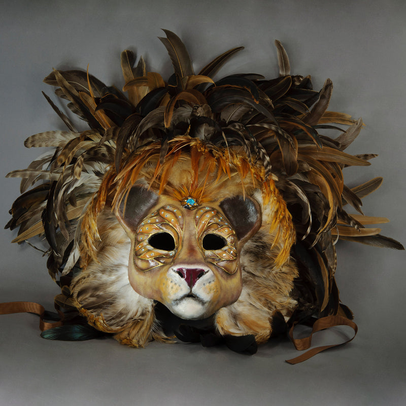 Stunning Lion Mask with a luxe crest of natural coque and assorted pheasant plumage. Embellished with Swarovski crystals, and assorted polished gem stones. Sure to turn heads at any costume, masquerade or Halloween party!  Hand-made in the USA using traditional Venetian paper-mache technique. Lined with hypoallergenic stretch velvet for comfort. Front view.